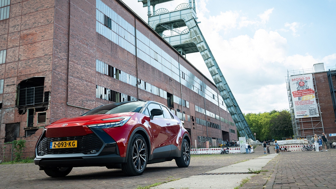 Toyota-C-HR-exterieur-vooraanzicht-roodkleurig-voor-gebouw-op-industriegebied